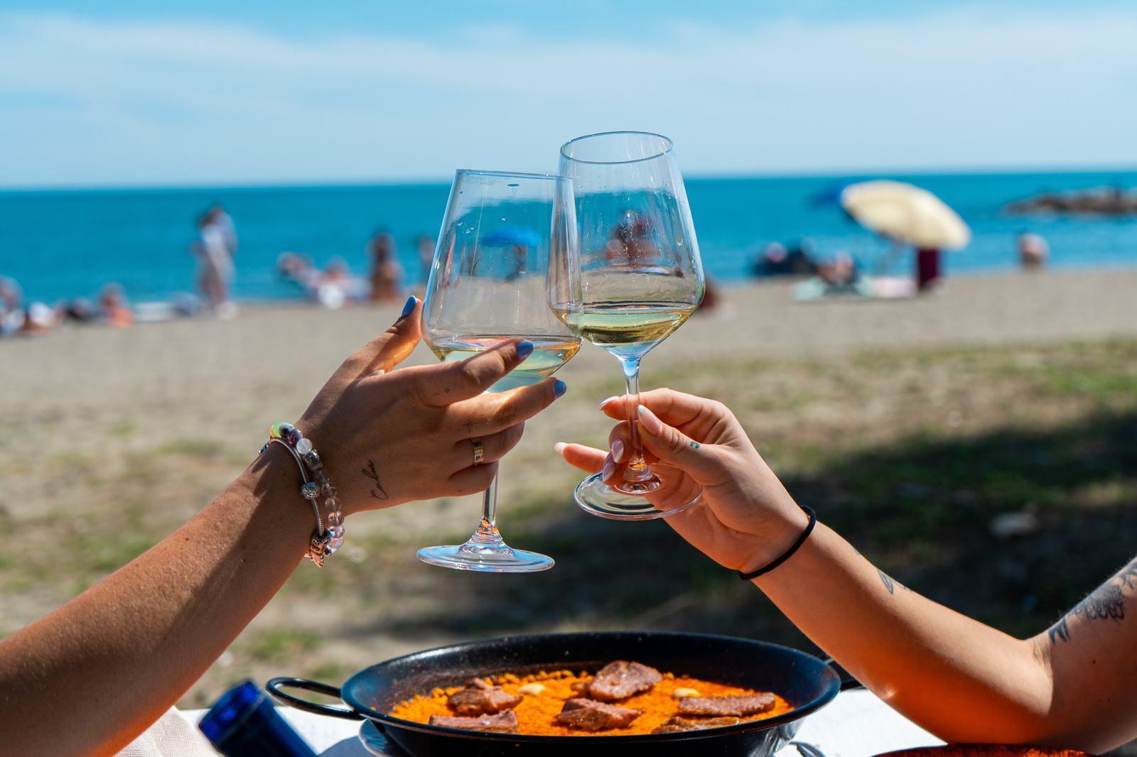 Brindis frente al mar con una paella en la mesa